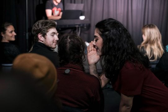 Woman whispering into an audience member's ear